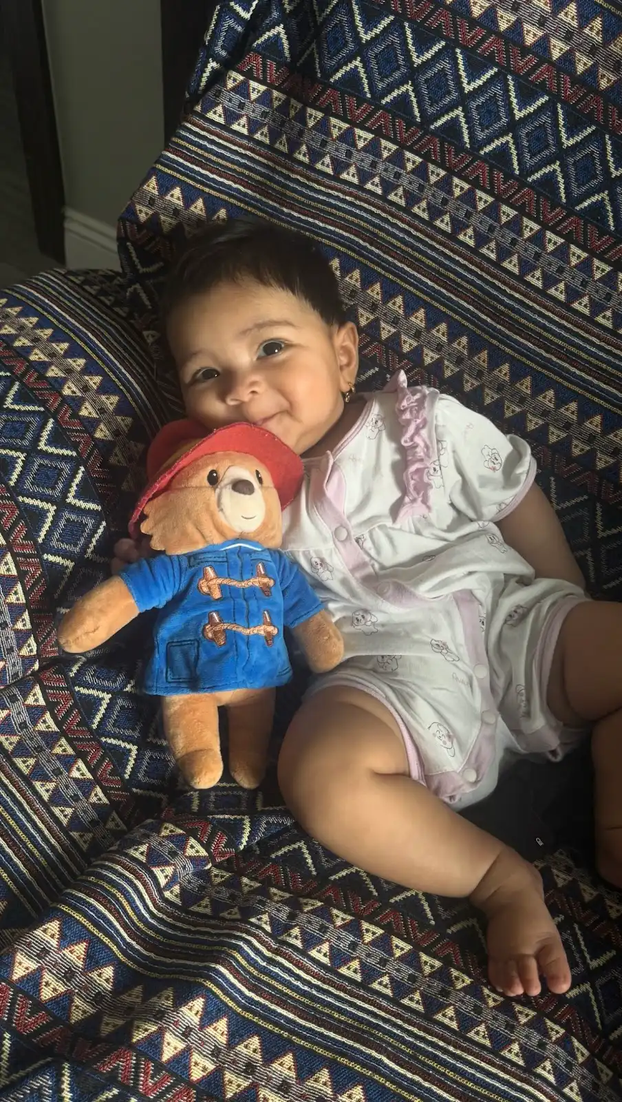 Châu Sa smiling, holding her Paddington Bear, sitting on a patterned chair
